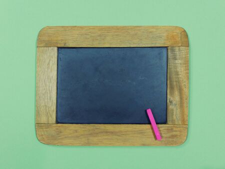 Blank vintage slate chalkboard and pink chalk pastel on green background.の写真素材