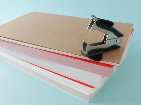 Black staple remover with brown notebook and books on bright blue background. 1の写真素材