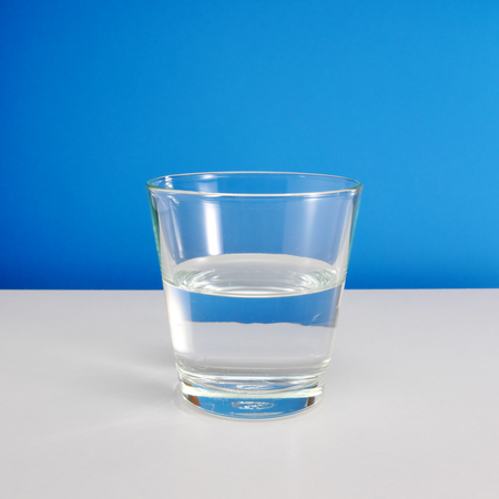 Half empty or half full glass of water on white table on blue background. 2の写真素材