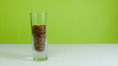 Whole grain traditional Thai red jasmine rice in small shot glass on white table on lemon green tone background.の写真素材
