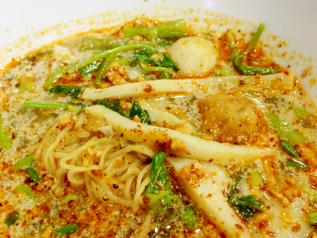 The close up of Thai Tom Yum spicy egg noodle soup with fish ball on white bowl.