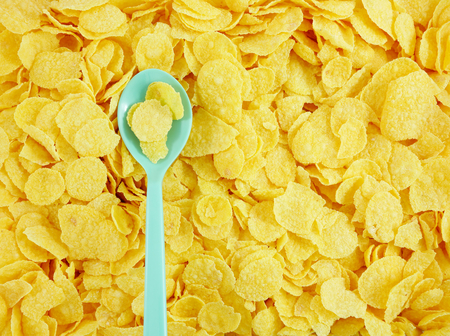 The close up of tasty golden corn flakes and plastic spoon.