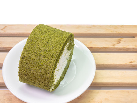 The close up of homemade matcha green tea cream roll soft cake dessert food with wood plank on white background.の写真素材