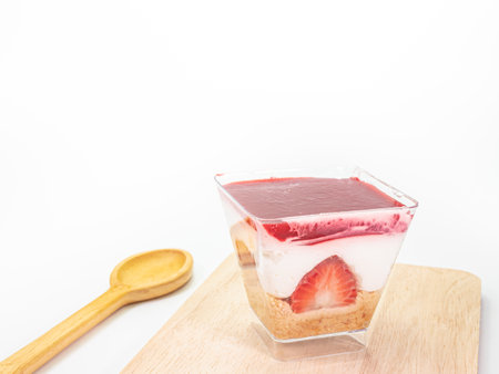 The close up of strawberry cheesecake in transparent plastic square shape cup with wood spoon on wooden plankの写真素材