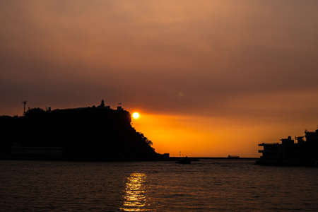 Sunset and sunlight at Kaohsiung harbor, a landscape of mountain with lighthouse and coastline silhouette colorful background in kaohsiung city, Taiwan.の写真素材
