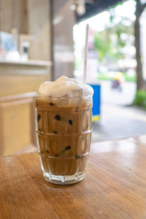 Thai iced coffee, a close up of glass of milk coffee cold drink beverage and white straw on wooden table at Thai food restaurant background in Bangkok, Thailand.の写真素材