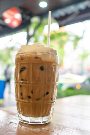 Thai iced coffee, a close up of glass of milk coffee cold drink beverage and white straw on wooden table at Thai food restaurant background in Bangkok, Thailand.の写真素材