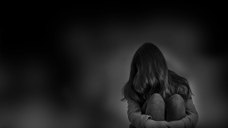 sad woman hug her knee and cry. Sad woman sitting alone in a empty room.の写真素材