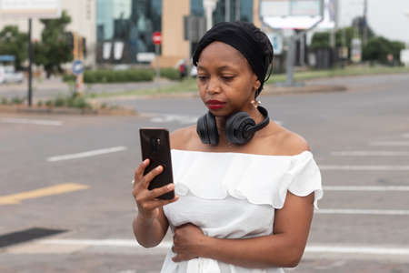 Unsmiling African woman taking a selfie with a smartphone with black headphones.