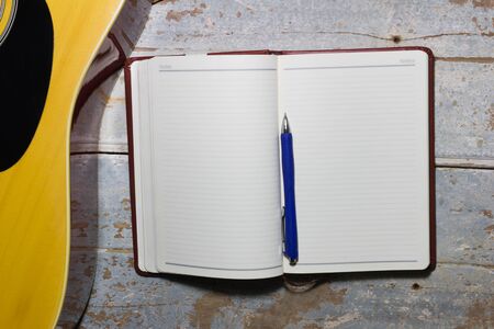 Notebook and blue pen with guitar on old wooden background,Writing musicの写真素材