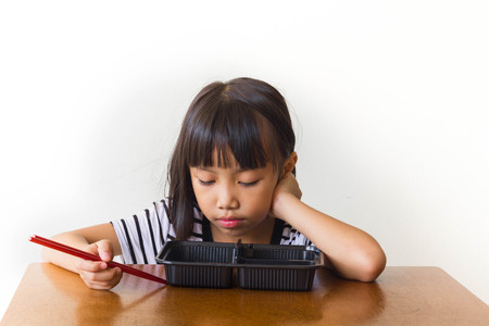 Bored children girl with red chopsticks sitting at the tableの写真素材