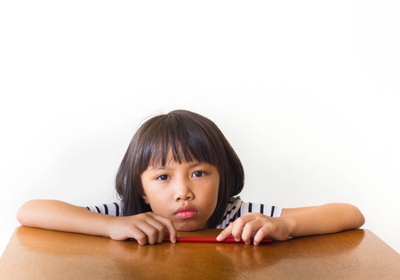 Bored children girl with red chopsticks sitting at the tableの写真素材