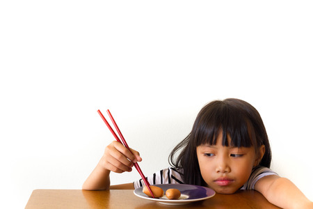 Bored children girl with red chopsticks sitting at the tableの写真素材