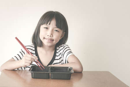 Joyful children girl with red chopsticks sitting at the table - Vintage Filter Effectの写真素材