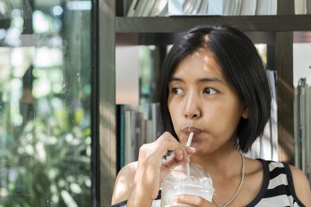 Asian woman in white and black shirts drinking coffee in the cafeの写真素材