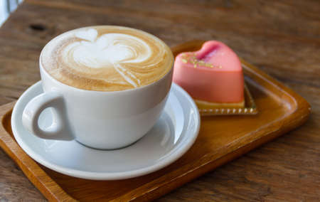 Close up cup of Coffee, latte on the wooden table with mousse rose cake heart shapedの写真素材