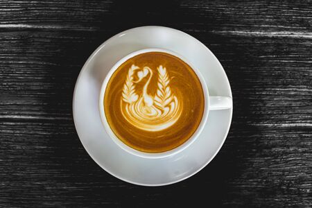 Close up white cup of Coffee, latte with beautiful latte art on the black wood background.の写真素材