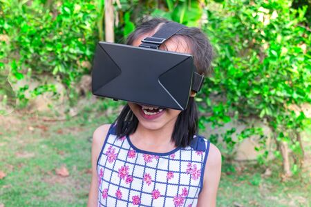 Adorable asian kid with virtual reality playing in a nature outdoors.