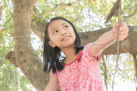 Close up happy adorable asian children wear red dress joyful with climbing trees .の写真素材