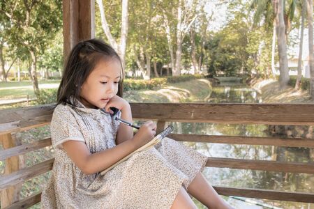 Adorable asian kids wear brown floral dress and joyful drawing in the park.の写真素材