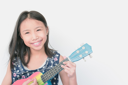 Selective focus beautiful little girl smiling with confidence and playing ukulele on white background. Concept child confidence.の写真素材