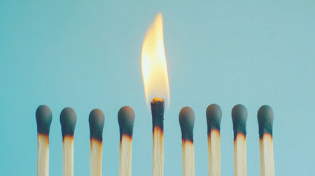 A single match burning against a line of untouched matches, showcasing the beauty of individuality and creation.の素材
