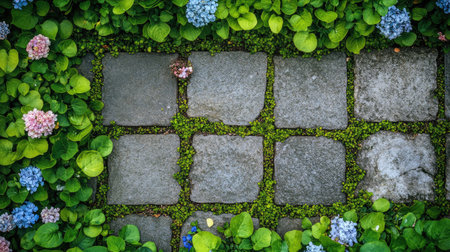 Top-down view of a bright green front lawn with artistic stone patterns and blooming flowers along the border.の素材