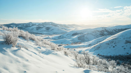 Snow-covered hills and mountains with a clear blue sky above and soft sunlight shining downの素材