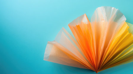 An artistic display of layered paper fan in vibrant orange and yellow colors set against a calming blue background, ideal for creative projects and inspirations.の素材