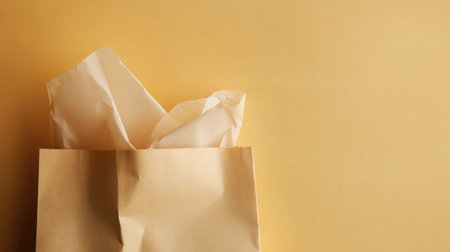 This image features a brown paper bag filled with white tissue paper set against a vibrant yellow background, perfect for showcasing packaging or gift ideas.の素材