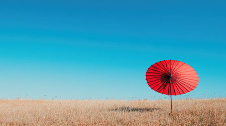A striking red umbrella stands alone in a golden field beneath a clear blue sky, capturing the essence of solitude and the serene beauty found in nature's simplicity.の素材
