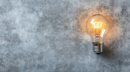 A vintage light bulb casts a warm glow against a textured concrete wall, enhancing interior spaces with style and ambiance. Perfect for design and decor projects.の素材