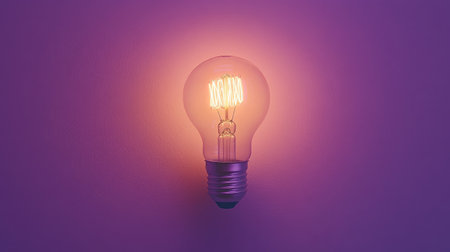 A vintage light bulb casts a warm glow against a purple wall, creating a cozy atmosphere perfect for any interior design project or home decor setting.の素材