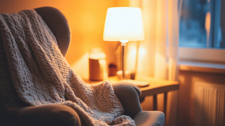 Close-up of a cozy corner with a rocking chair, a baby blanket draped over it, and a glowing lamp in the background. No people included.の素材