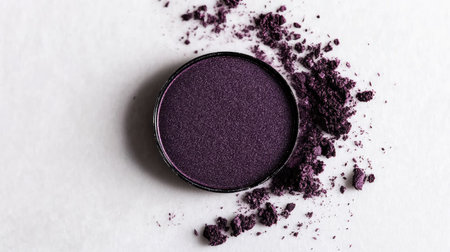 A single round eyeshadow pan in deep purple, surrounded by subtle dust traces on a clean white surface.の素材