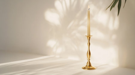 A sleek gold candlestick with a tapered candle, its shadow softly cast on the white surface.の素材