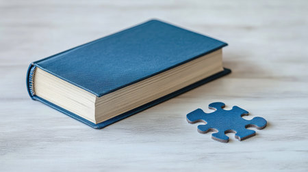 Educational concept with a blue book and a puzzle piece, both placed together on a light background, representing critical thinking and learningの素材