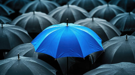 A blue umbrella standing out in a crowd of black umbrellas.の素材