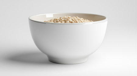Simple white bowl with a few scattered grains of rice, set on a solid white background for a clean look.の素材