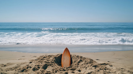 A tranquil beach setting featuring a surfboard partially buried in sand, with gentle ocean waves lapping at the shore, ideal for summertime and beach-related themes.の素材