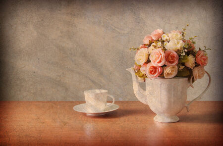 Abstract old background with romantic a bouquet of roses in white  jug with coffee cup on wooden table and concrete walls.For art texture, grunge design, and vintage cement wall or border frameの写真素材