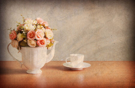 Abstract old background with romantic a bouquet of roses in white  jug with coffee cup on wooden table and concrete walls.For art texture, grunge design, and vintage cement wall or border frameの写真素材