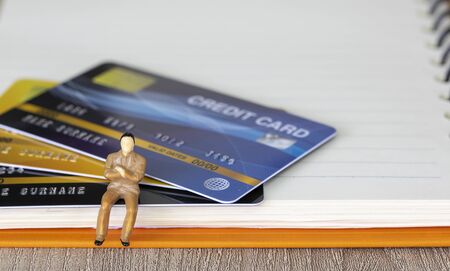 Figure miniature businessman or small people sit on credit card and book background for money and financial business shopping concept.の写真素材