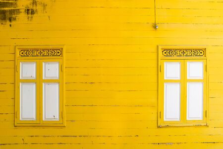 yellow peeling painted on wooden wall with white window, textures background, cracked paint