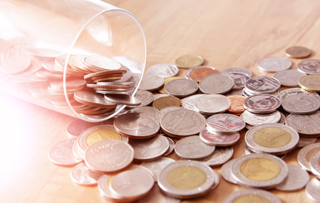 Concept of saving money. The money coin is scattered from a glass bottle on the wood background.の写真素材