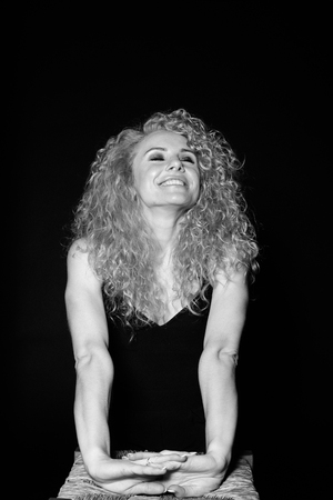 Close up studio portrait of a pretty curly blonde woman, eyes closed, hands together, against plain studio backgroundの写真素材
