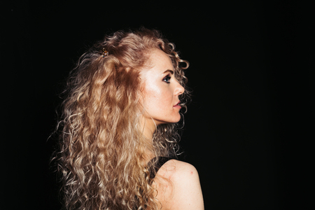 Close up studio portrait of a pretty curly blonde woman, wearing black dress, looking to the side, against plain studio backgroundの写真素材