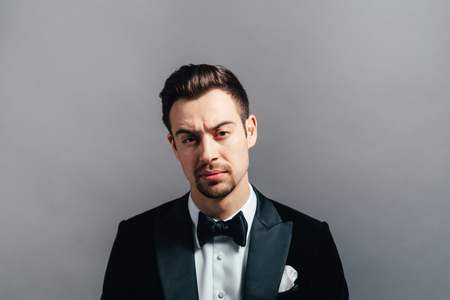 Portrait of a young handsome man in a dinner jacket,  seriously looking at the camera, against plâain studio background.の写真素材