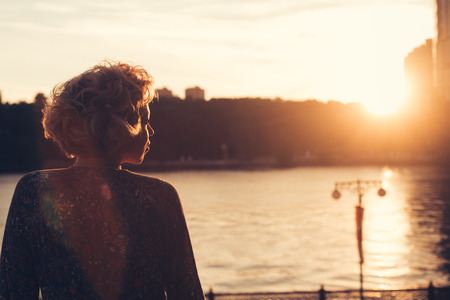 Woman watching the sunset in a park on the river bankの写真素材