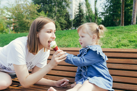 Portrait of a young mother and her 3 years old daughter eating ice cream in a city park on a warm sunny dayの写真素材